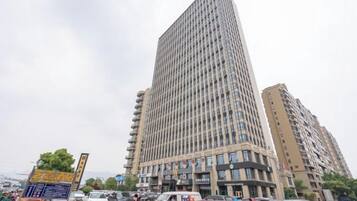 A tall, modern building with a grid-like facade, surrounded by other buildings and parked cars.