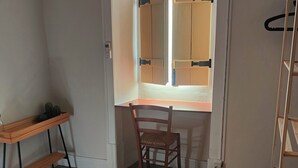 Une pièce avec un bureau en bois, une chaise et une fenêtre équipée de stores.