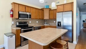 A modern kitchen with wooden cabinets, stainless steel appliances, and a central island with stools. - Beautiful, 3 bed, 2 bath, Cozy Condo just minutes from Boardwalk & Beach Access! (Wildwood)