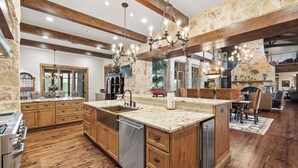 A spacious kitchen with wooden cabinets, a large island, and a stone accent wall. - Private Ranch - Pool, Ping Pong, Yoga, Weddings, Games (Bergheim)