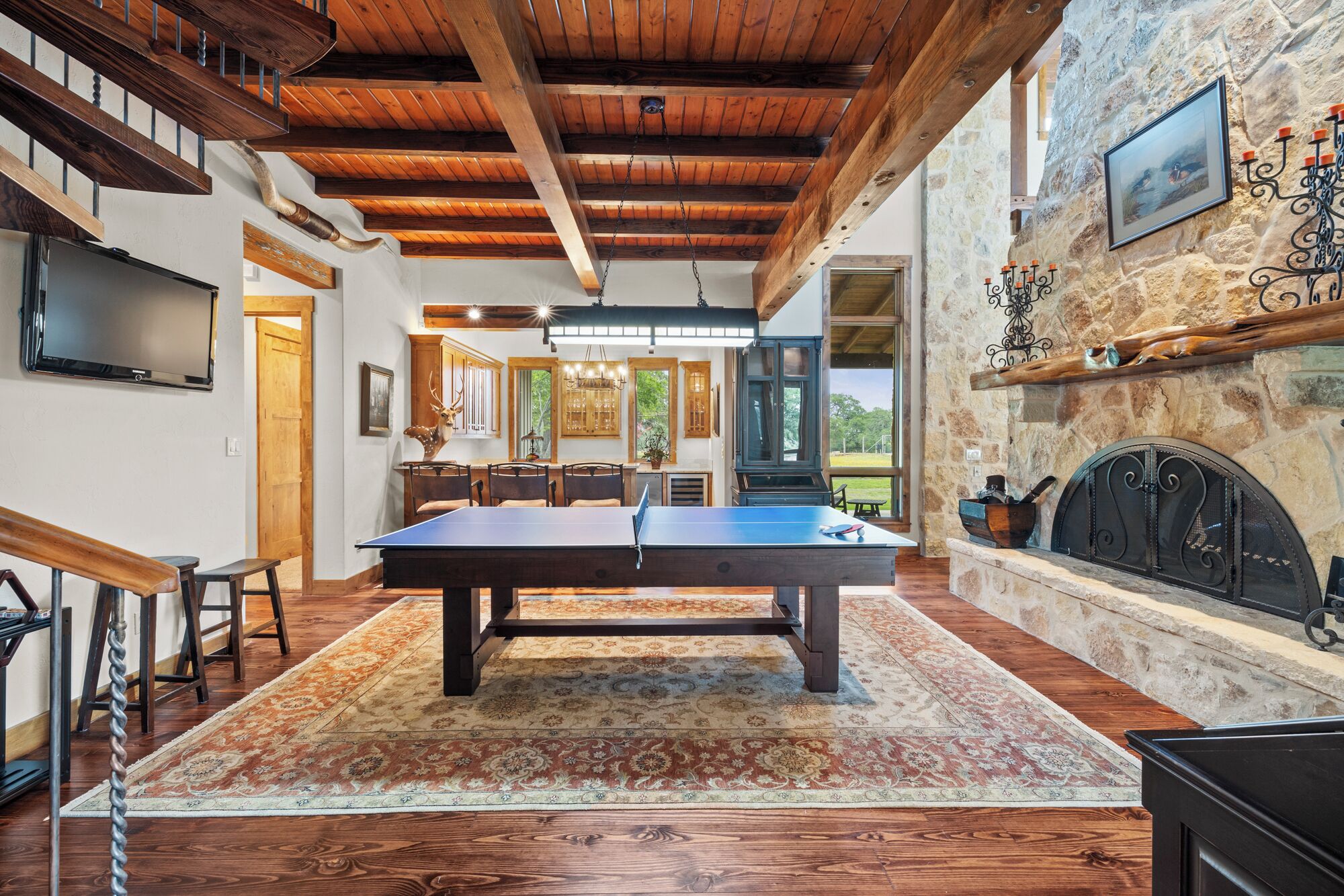 A spacious room with a pool table, wooden flooring, and a stone fireplace.