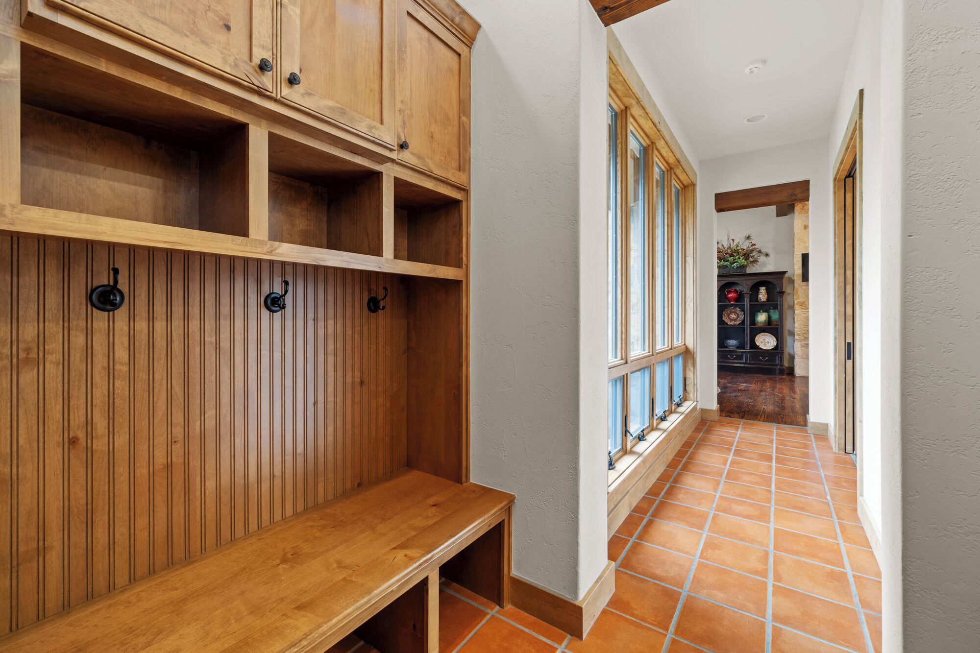 A hallway with wooden paneling, a bench, and a display cabinet with decorative items.