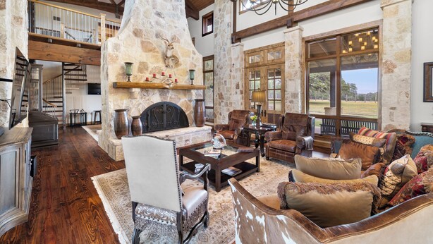 A spacious living room with a stone fireplace, leather furniture, and large windows offering a view of the outdoors. - Private Ranch - Pool, Ping Pong, Yoga, Weddings, Games (Bergheim)
