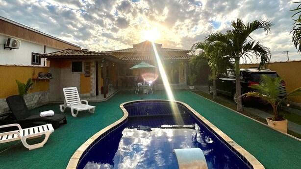 A swimming pool with a sunlit sky and clouds in the background. - Casa 6 pessoas com Piscina (Sao Pedro da Aldeia)