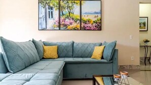 A living room with a sectional sofa, a coffee table, and a wall-mounted painting. - Casa 6 pessoas com Piscina (Sao Pedro da Aldeia)