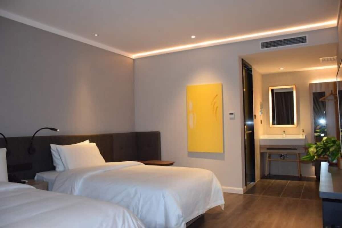 A hotel room with two beds, a bathroom with a mirror and sink, and a plant.