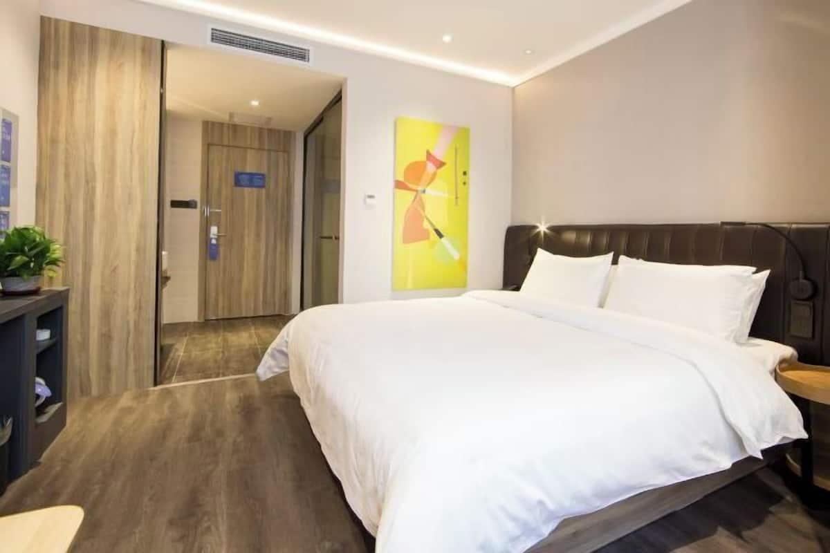 A hotel room with a bed, a nightstand, a desk, and a door leading to another room.