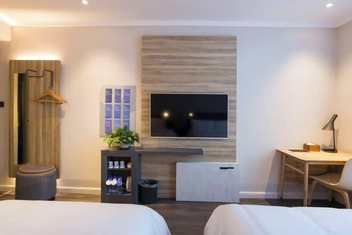 A modern hotel room with a bed, a desk, a TV, a plant, and a wooden wall panel.