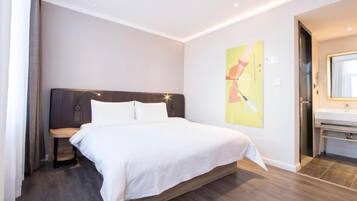 Une chambre d’hôtel moderne dotée d’un grand lit, d’une table de chevet, d’une œuvre d’art accrochée au mur et d’une salle de bain avec un lavabo et un miroir.