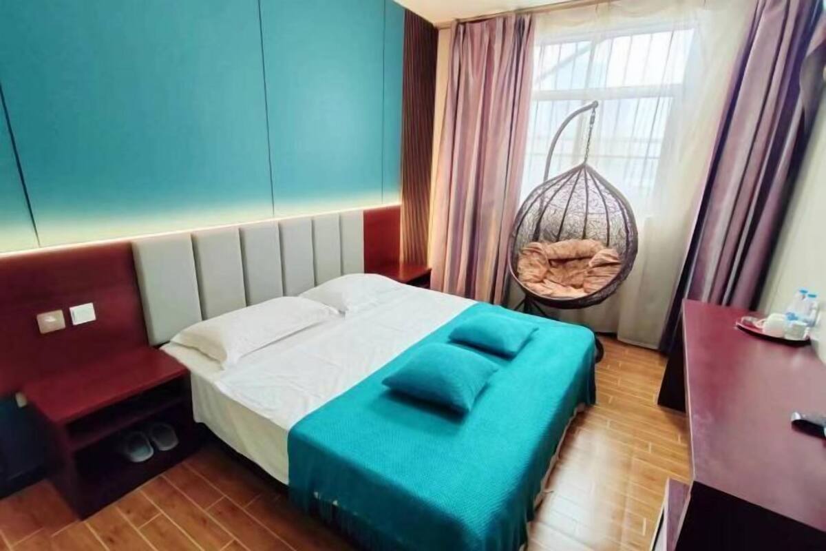 Habitación de hotel con cama, una sillona colgante, escritorio y ventana con cortinas.