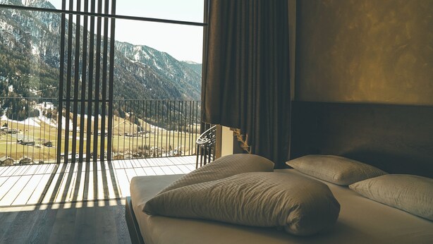 A bedroom with a large window, a bed with pillows, and a view of mountains.