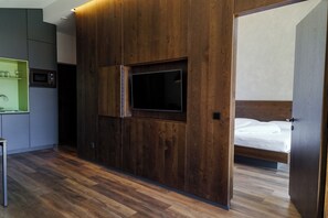 Ein modernes Hotelzimmer mit Holzwand, Flachbildfernseher, Bett und einer kleinen Küchenzeile.