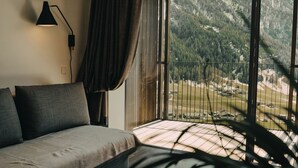 A bedroom with a bed, a lamp, a view of a mountainous landscape through a balcony.