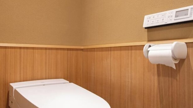 A toilet with a white lid, a toilet paper holder, and a digital control panel on the wall. - Hiyori Gojo (Kyoto)
