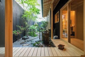 A traditional Japanese-style courtyard with a wooden deck, a stone water feature, and a wooden building with sliding doors. - Hiyori Gojo (Kyoto)