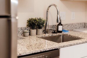 A kitchen with granite countertops, a stainless steel sink, and a dishwasher. There are small potted plants on the counter.