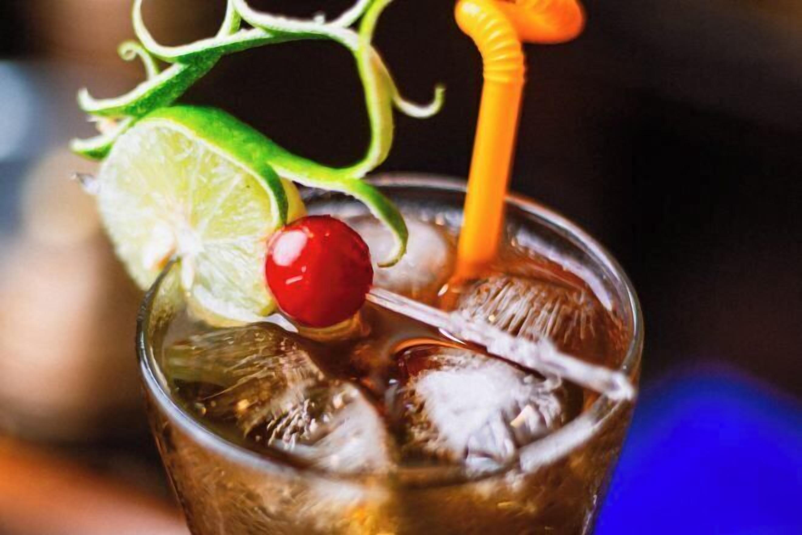 A glass with ice cubes, a lime slice, a cherry, and a straw.