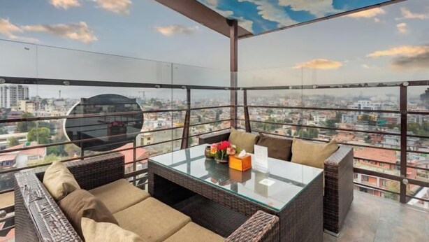 A high-rise balcony with a glass table and wicker furniture, overlooking a cityscape. - Hotel Kutumba (Lalitpur)