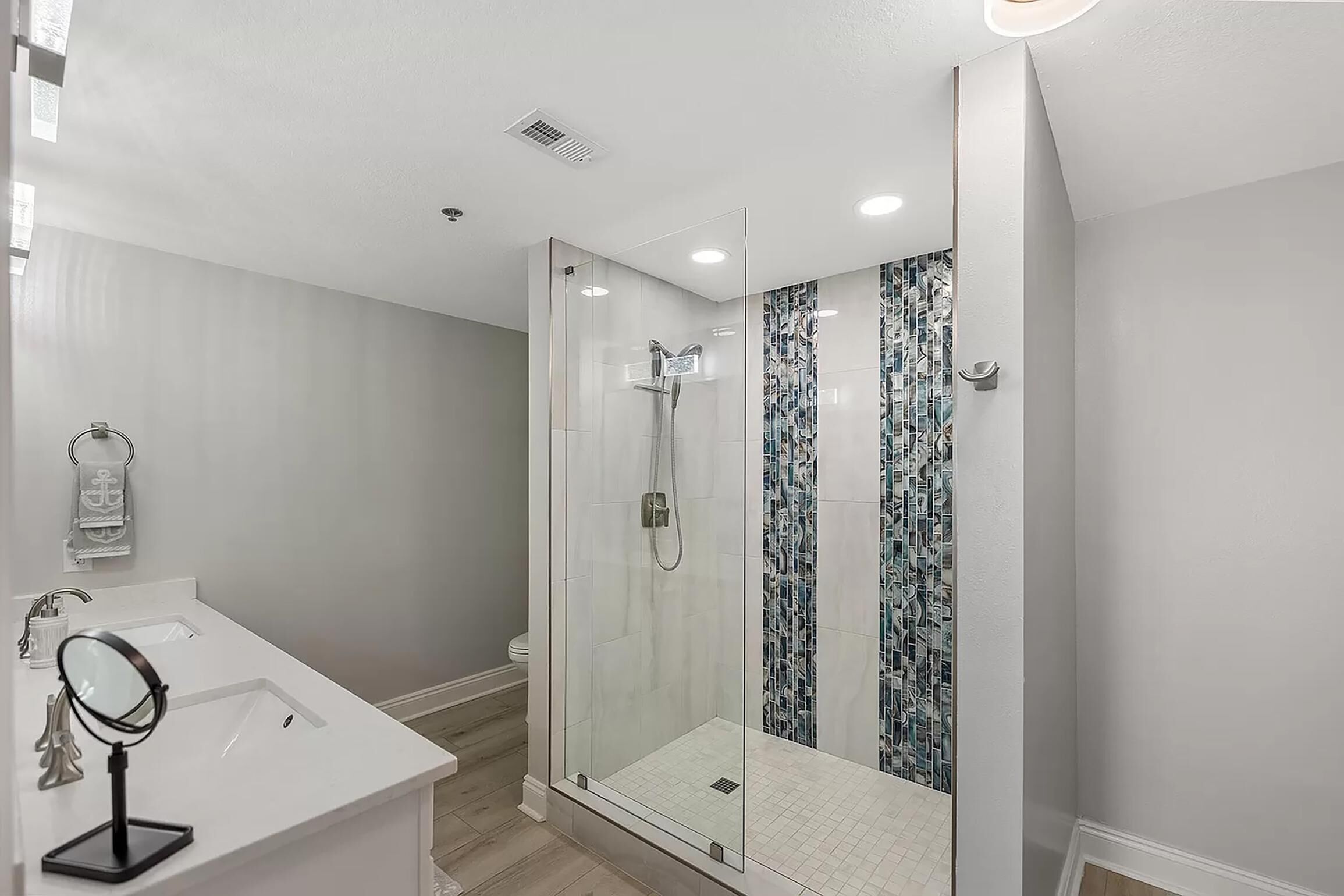 A modern bathroom with a glass-enclosed shower, a white sink with a mirror, and a tiled backsplash.