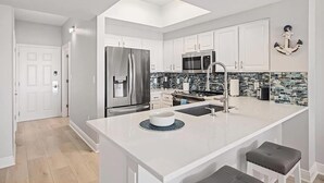 A modern kitchen with white cabinetry, a stainless steel refrigerator, a microwave, and a large island with a sink.
