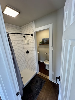 Un baño moderno con paredes de ladrillo blanco, una zona de ducha con toallero negro, un inodoro y un pequeño estante con una planta.