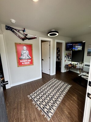 Ein Flur mit Holzboden, einem gemusterten Teppich, einem Buddha-Poster, einer Deckenleuchte und einem an der Wand montierten Fernseher.