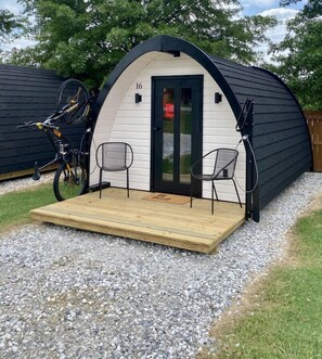 A small, single-room structure with a wooden deck, two chairs, and a bicycle parked outside. - The Bike Inn #16, White River Cabin (Bentonville)