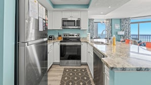Una cocina moderna con electrodomésticos de acero inoxidable, armarios blancos, encimera de mármol y vista al océano.