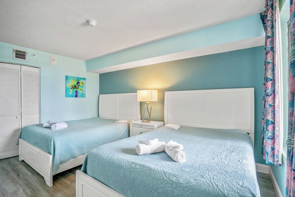 A hotel room with two beds, a nightstand with a lamp, a painting on the wall, and a window with curtains.