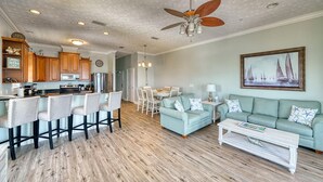 A spacious living area with a light blue sofa, a coffee table, and a dining area with a white table and chairs. - Vista del Mar I - Short Walk to the Beach 301 (Panama City Beach)