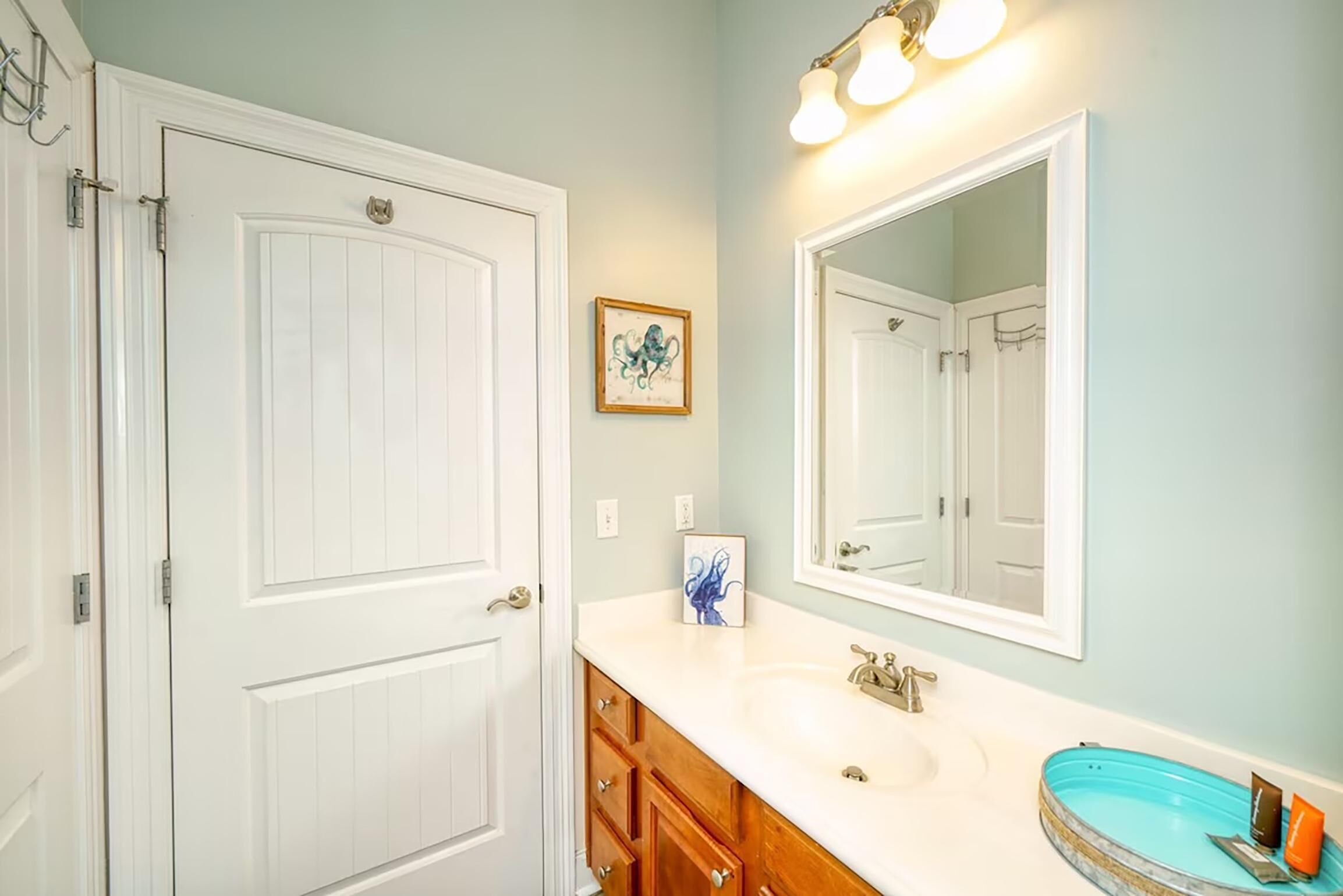 A bathroom with a white door, a white sink, a mirror, and a blue bathtub.