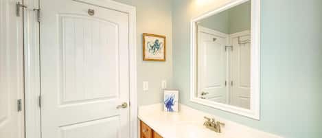 A bathroom with a white door, a white sink, a mirror, and a blue bathtub.