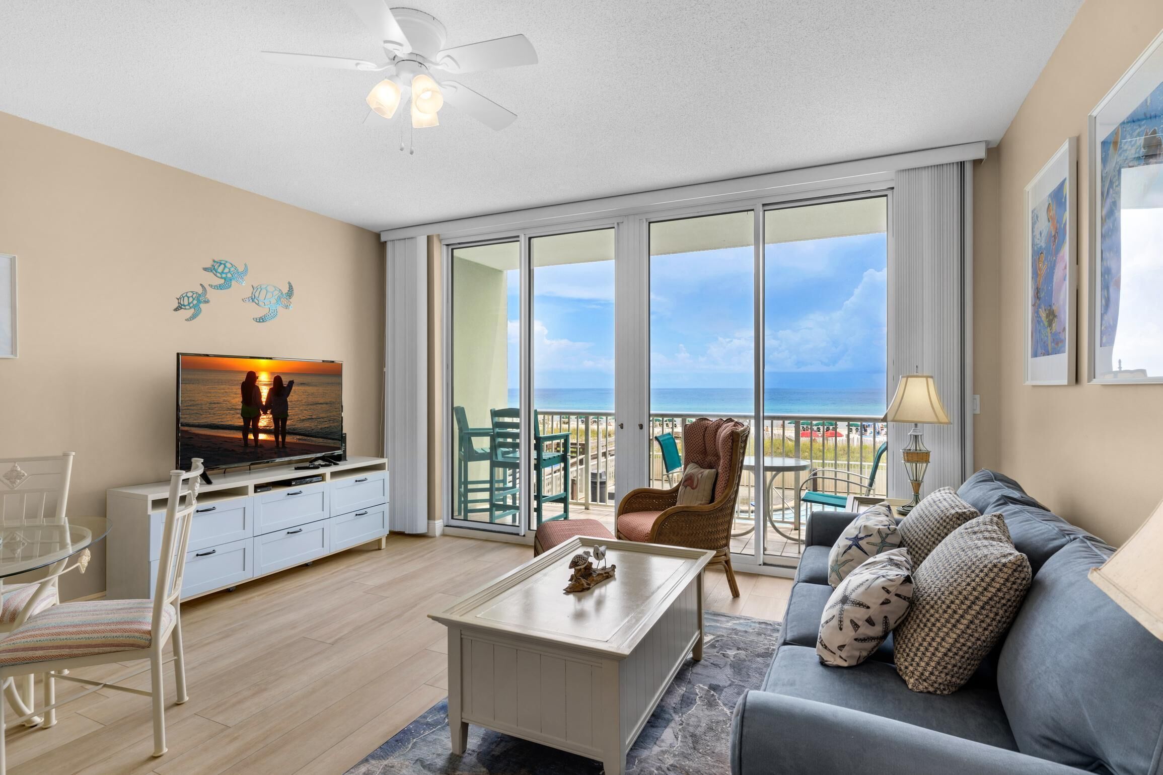 A spacious living room with a TV, a coffee table, a sofa, and a balcony with a view of the ocean.