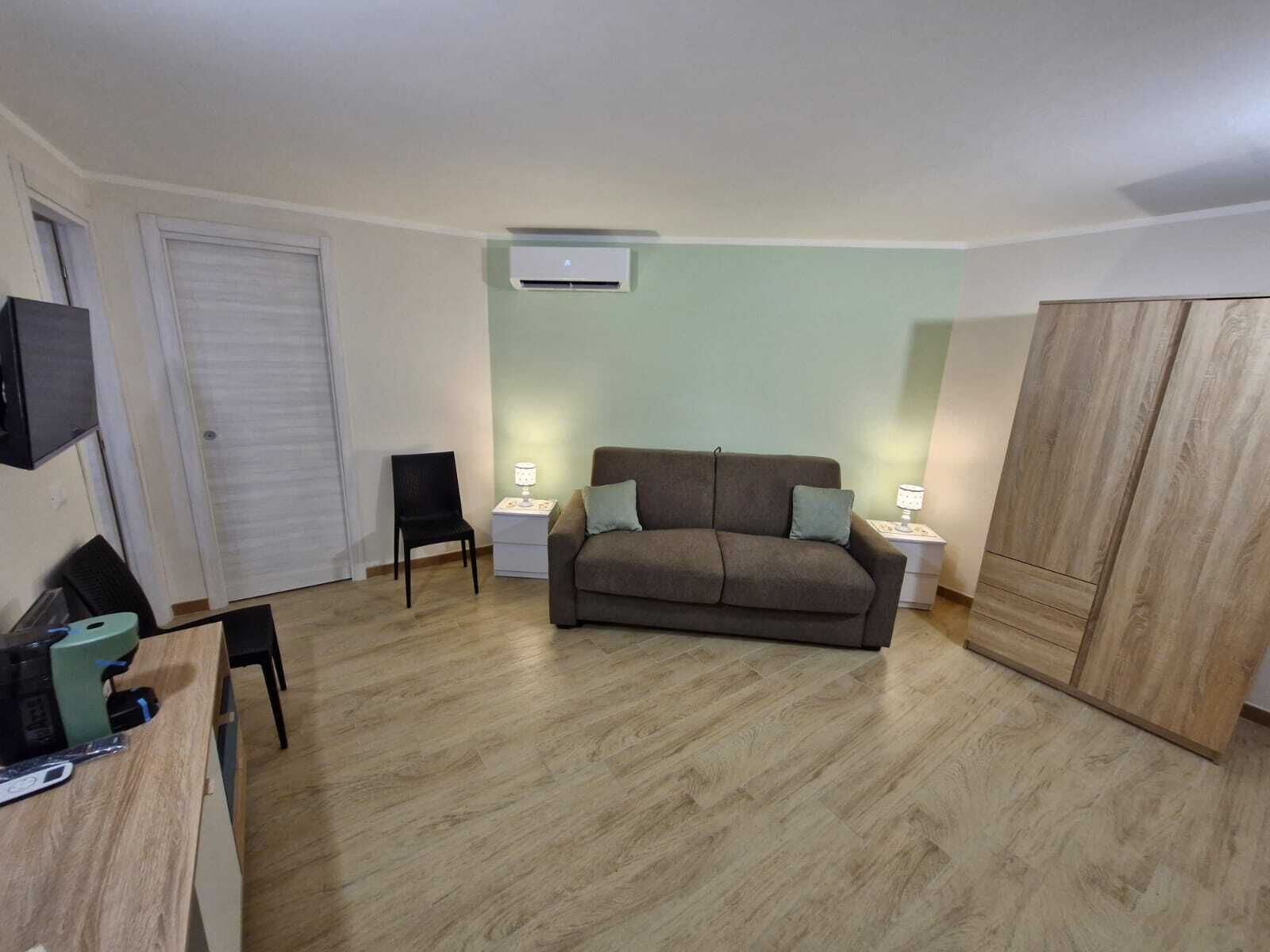 A small, well-lit room with a sofa, a chair, a desk, and a wardrobe.
