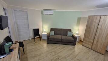 A small, well-lit room with a sofa, a chair, a desk, and a wardrobe.