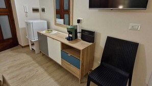 A compact living space with a wooden desk, a black chair, a television mounted on the wall, and a refrigerator. - Medea Appartamenti (Siracusa)