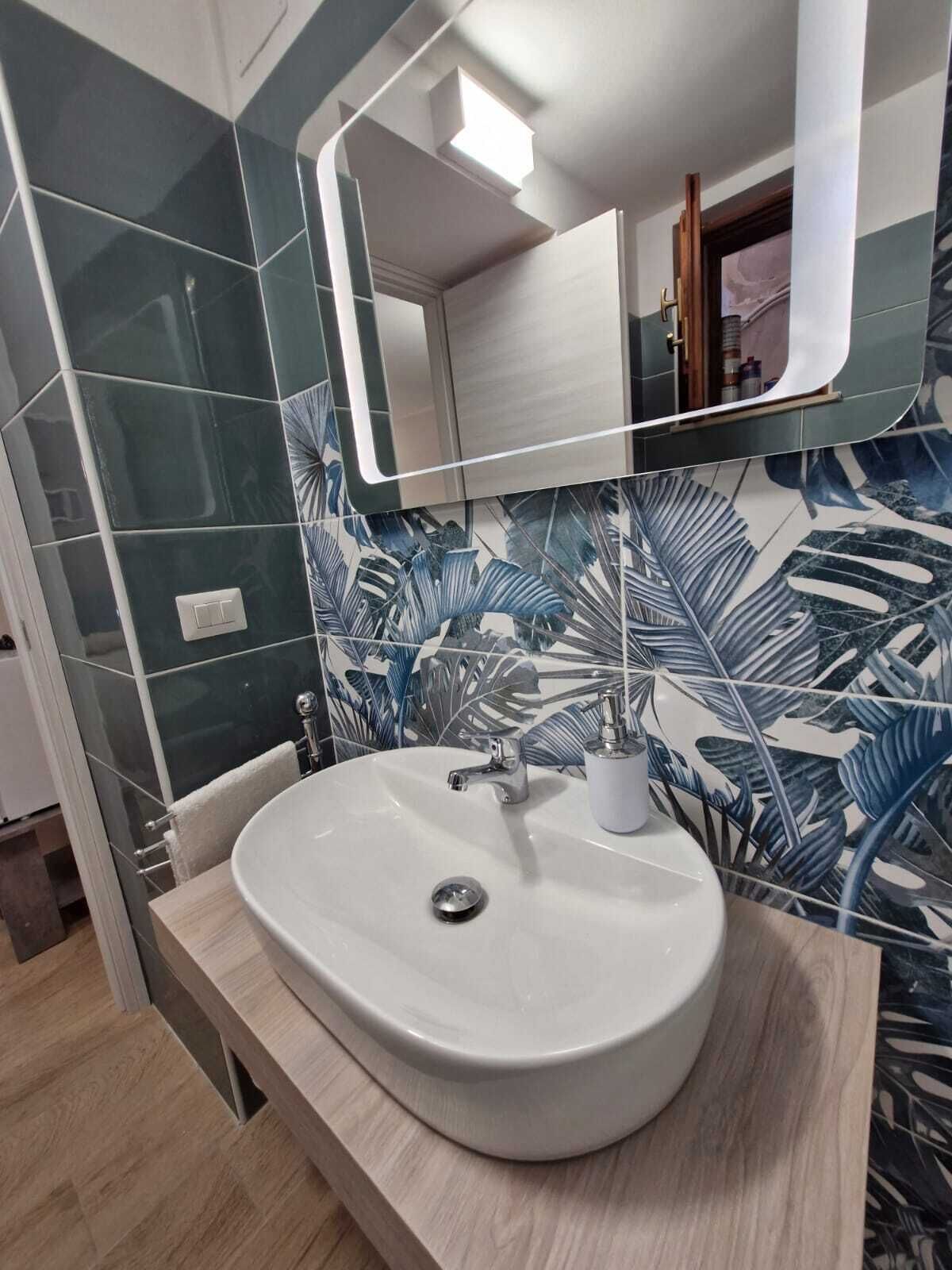 A bathroom with a white sink, a mirror, and a wall with a tropical leaf pattern.