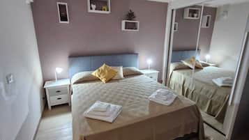 Une chambre à coucher avec un grand lit, des tables de chevet, un miroir et une petite étagère ornée d’objets décoratifs.