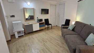 Un espace de vie compact comprenant un canapé marron, un petit bureau avec un miroir, une télévision et une armoire blanche.