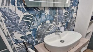 A bathroom with a white sink, a wooden vanity, and a mirror above the sink. - Medea Appartamenti (Siracusa)