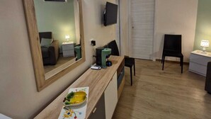 A compact living space with a kitchenette, a mirror, a flat-screen TV, a small dining table, and a chair. - Medea Appartamenti (Siracusa)