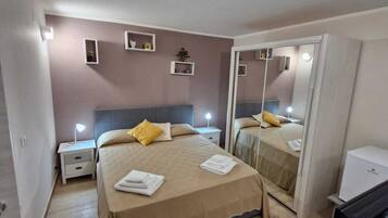 A hotel room with a bed, bedside tables, a mirror, a desk with a computer, and a small plant on the wall.