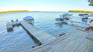 A wooden dock extending into calm water, with boats docked and a covered area with chairs.