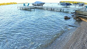 A lakeside dock with a covered boat, chairs, and a rocky shoreline.