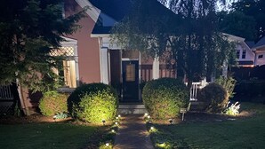 A pathway lined with evenly spaced lights leading to a house with a dark front door and a small sign reading "NCA" on the right.