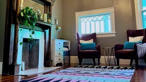 A living room with a fireplace, two armchairs, a patterned rug, and a chandelier.
