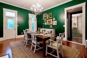 Un comedor con mesa de madera y sillas blancas, paredes verdes y una lámpara de araña.