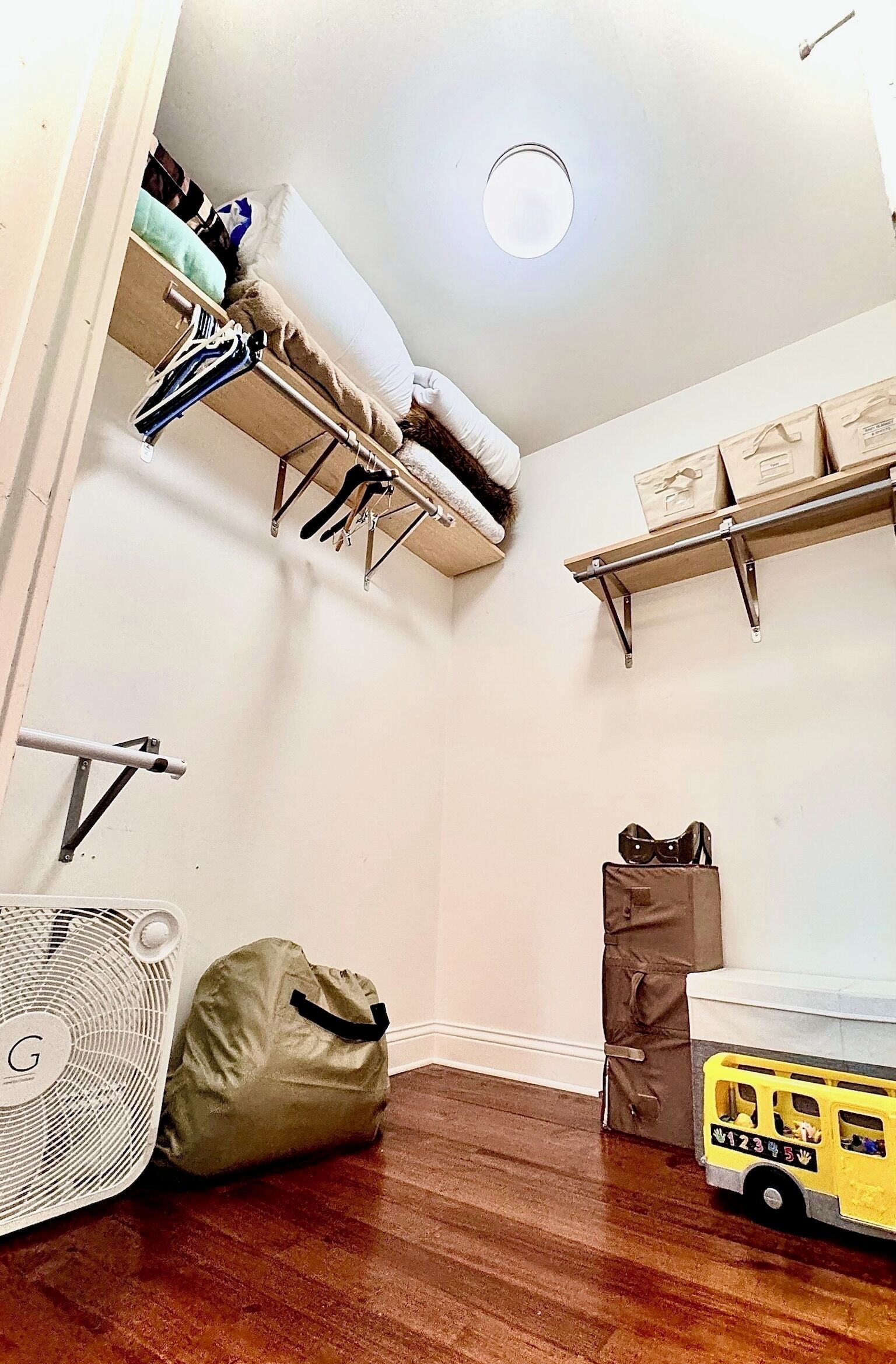 Une pièce avec un lit, un ventilateur, un sac et un petit bus jouet.