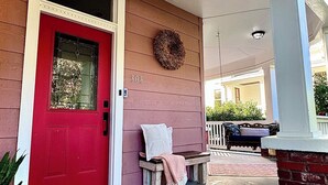 A red door with a wreath above it, a bench with a towel, and a brick wall.