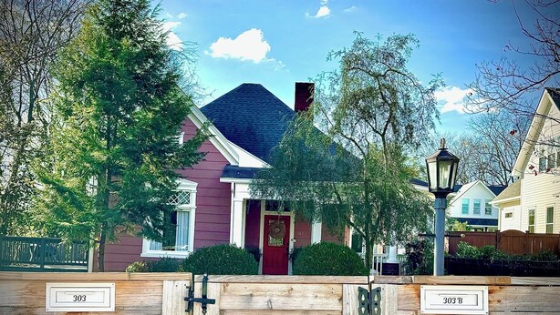 A residential house with a red door, a mailbox labeled '303', and a wooden fence.